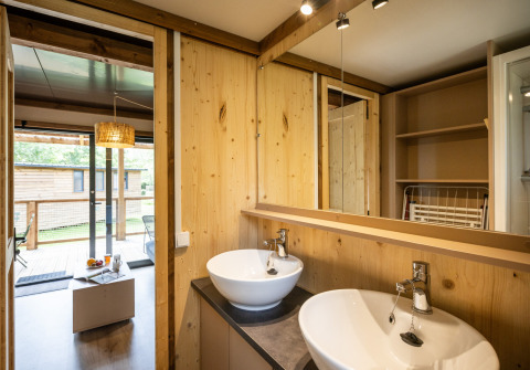 Moderne badeværelse i Chalet Portland glamping, med to håndvaske, trævægge og udsigt til terrasse.