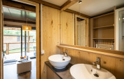 Baño moderno en Chalet Portland glamping, con dos lavabos, paredes de madera y acceso a terraza exterior.