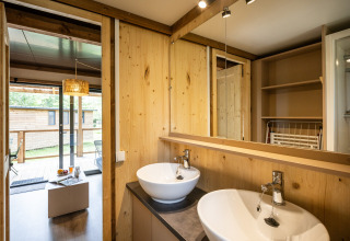 Moderne badeværelse i Chalet Portland glamping, med to håndvaske, trævægge og udsigt til terrasse.