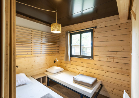 Cozy bedroom in Chalet Portland with two single beds, wooden walls, window, and warm lighting.