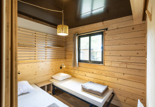 Cozy bedroom in Chalet Portland with two single beds, wooden walls, window, and warm lighting.