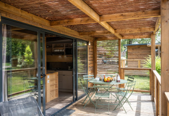 Overdekt houten terras van Chalet Portland met tafel, stoelen en ontbijt, zicht op de tuin.