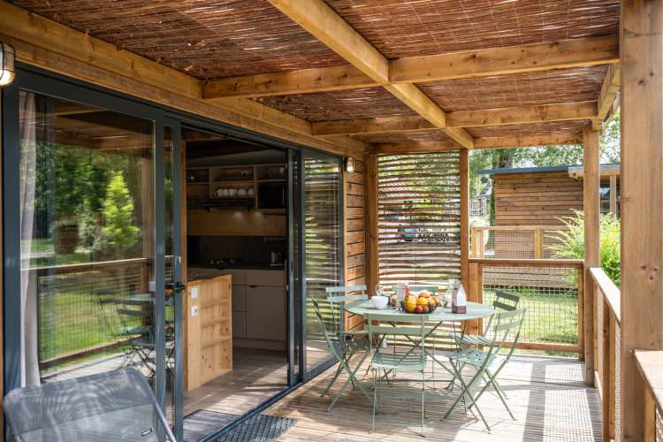 Terraza de madera en el Chalet Portland con mesa, sillas y desayuno, vista al jardín verde exterior.