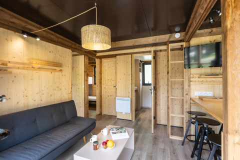 Alojamiento glamping Chalet Portland con interior de madera, sofá, mesa de bar, TV y detalles modernos.