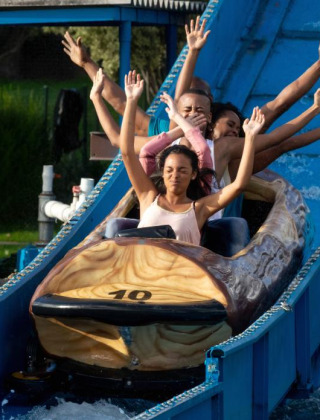 Cuatro personas disfrutan de un tobogán acuático en un parque vacacional con opciones de glamping.