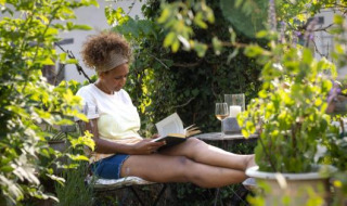 Frau liest entspannt ein Buch und genießt Wein im Grünen im Camping Huttopia De Veluwe, Niederlande.