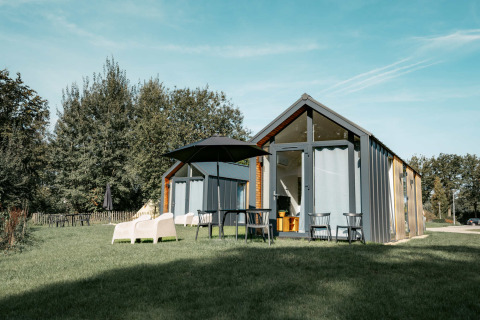 Moderne Ferienhütte mit Glasfront, Gartenmöbeln und Sonnenschirm auf Rasen im Camping de Italiaanse Meren, Gelderland.
