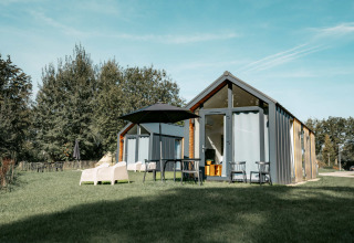 Moderne chalet met grote ramen, tuinmeubelen en parasol op gras bij Camping de Italiaanse Meren, Gelderland.