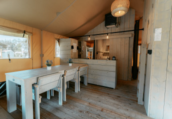Indvendigt billede af en hyggelig træhytte med spisebord, stole og køkken i Cottage på Camping de Italiaanse Meren.