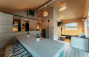 Interior rústico y luminoso de una cabaña en Camping de Italiaanse Meren en Países Bajos, con mesa y sofá.