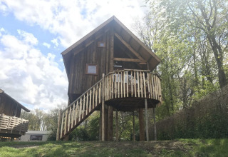 Treehouse named Ooievaarsnest at Camping de Koeksebelt in the Netherlands, surrounded by trees and sunlight.