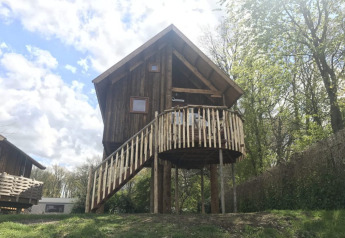 Træhus kaldet Ooievaarsnest på Camping de Koeksebelt i Holland, omgivet af grønne træer og solskin.