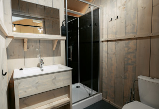Baño con paneles de madera, ducha, inodoro y lavabo en la cabaña de Camping de Italiaanse Meren, Países Bajos.