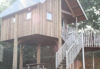 Casa sull’albero in legno su palafitte con terrazza e scale, al sole al Camping de Koeksebelt, Paesi Bassi.