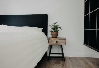 Soveværelse i Oslo Suite ved Camping de Italiaanse Meren med sort sengegavl og natbord med plante.