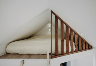 Cozy loft bed with wooden railing in the Oslo Suite tiny house at Camping de Italiaanse Meren, Netherlands.