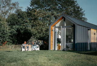 Two people relaxing outside the Oslo Suite tiny house at Camping de Italiaanse Meren in the Netherlands.