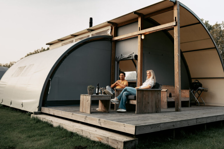 Zwei Personen entspannen auf der Veranda einer Arcade-Lodge auf Camping de Italiaanse Meren in den Niederlanden.