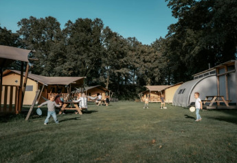 Børn leger på en grøn græsplæne foran Arcade Lodge på Camping de Italiaanse Meren i Holland.