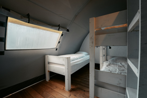 Indvendig udsigt af et soveværelse med enkeltseng og køjeseng på Arcade ved Camping de Italiaanse Meren.