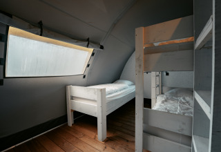 Indvendig udsigt af et soveværelse med enkeltseng og køjeseng på Arcade ved Camping de Italiaanse Meren.