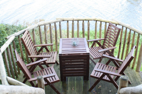 Terrazza di legno con quattro sedie e tavolo vista fiume a Ooievaarsnest, Camping de Koeksebelt, Paesi Bassi.