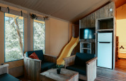 Indretning af Safari Lodge XL i Camping de Italiaanse Meren med træmøbler, gul rutsjebane og køleskab.