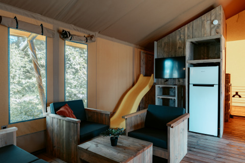 Interieur van Safari Lodge XL bij Camping de Italiaanse Meren met houten meubels, glijbaan en koelkast.