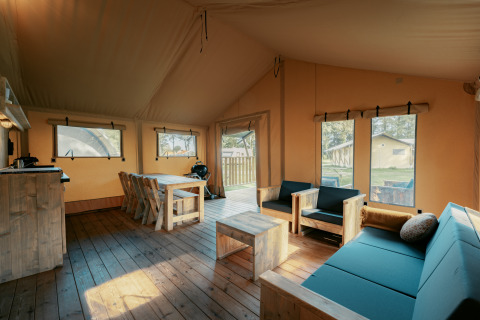 Interior de la amplia tienda safari Nomad XL en Camping de Italiaanse Meren, Países Bajos, con muebles rústicos.