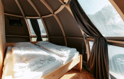 Indvendigt billede af en moderne, buet lodge med seng og store vinduer på Camping de Italiaanse Meren.