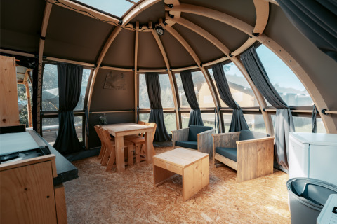 Interior de una cabaña redonda con muebles de madera y grandes ventanales en Panorama de Camping de Italiaanse Meren, Países Bajos.
