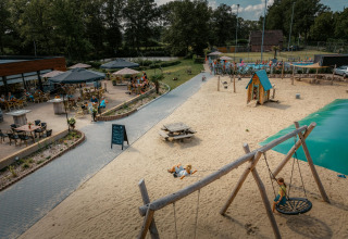 Kinder spielen am Sandstrand bei Camping de Italiaanse Meren, mit Café-Terrasse und Gästen im Hintergrund.