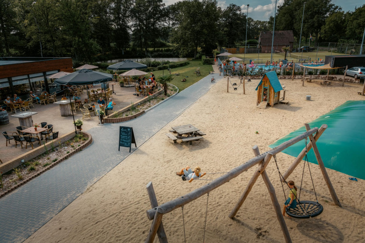 Kinder spielen am Sandstrand bei Camping de Italiaanse Meren, mit Café-Terrasse und Gästen im Hintergrund.