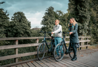 Zwei Personen entspannen mit ihren Fahrrädern auf einer Brücke im grünen Camping de Italiaanse Meren, Gelderland.