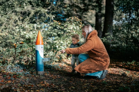 Vrouw en kind verkennen een beschilderd houten figuur in het bos bij Camping de Italiaanse Meren, Gelderland.