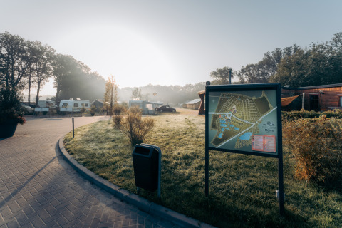 Camping de Italiaanse Meren in Gelderland, Netherlands, showing caravans, a site map, wooden cabins and morning sunlight.