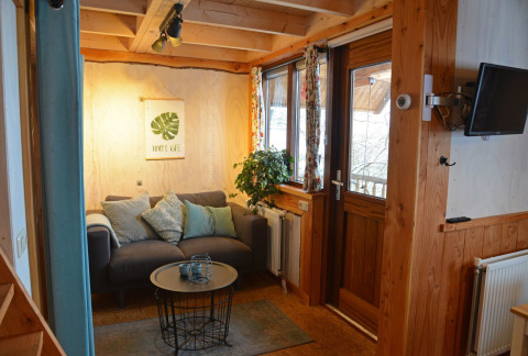 Cozy treehouse living room at Ooievaarsnest, Camping de Koeksebelt, with sofa, pillows, and plants.
