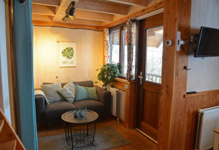 Cozy treehouse living room at Ooievaarsnest, Camping de Koeksebelt, with sofa, pillows, and plants.