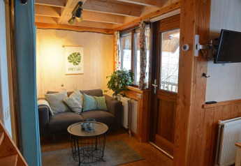 Træhusets hyggelige stue med sofa, puder, planter og plads til afslapning på Camping de Koeksebelt.