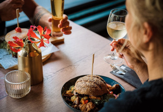 Due persone gustano hamburger e vino al Camping de Italiaanse Meren, parco vacanze in Gheldria, Paesi Bassi.