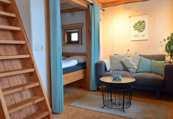 Cozy living area with sofa and wooden stairs in the Ooievaarsnest tree house at Camping de Koeksebelt, Netherlands.