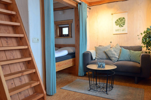 Hyggelig stue med sofa og trappe i træhusset Ooievaarsnest på Camping de Koeksebelt, Holland.