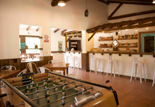 Sala interior en Huttopia Parque de Doñana, Andalucía, con futbolín, barra de bar y zona de comedor.