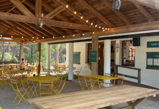 Buitenruimte van Huttopia Parque de Doñana met houten tafels, gele stoelen en gezellige lichtslingers.