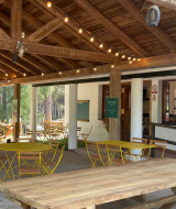 Outdoor café at Huttopia Parque de Doñana with wooden tables, yellow chairs, and string lights in Andalusia.