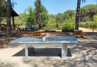 Tischtennisplatte im Freien bei Huttopia Parque de Doñana, umgeben von Bäumen und Picknicktischen in Andalusien.