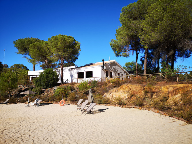 Zandstrand met ligstoelen en parasols voor vakantiewoningen en pijnbomen bij Huttopia Parque de Doñana, Andalusië.