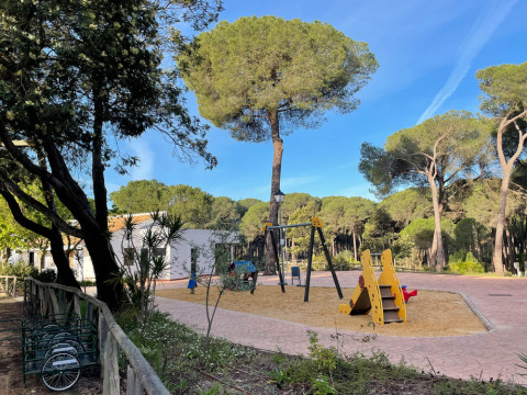Parque infantil con columpios y tobogán rodeado de árboles en Huttopia Parque de Doñana, Andalucía, España.