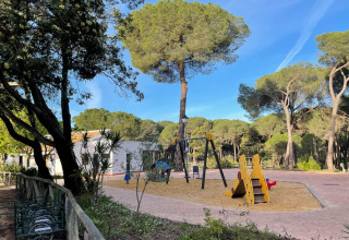 Speelplein met schommels en glijbaan omringd door bomen in Huttopia Parque de Doñana, Andalusië, Spanje.