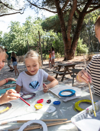 Children enjoy outdoor painting activities under trees at Huttopia Parque de Doñana in Andalusia, Spain.
